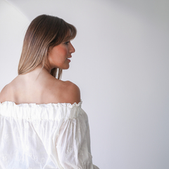 Blusa Allison off-shoulder en color blanco, con detalles de bordado, vista lateral de una modelo.