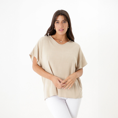 Modelo luciendo una blusa de color beige, con mangas cortas y un diseño sencillo, combinada con pantalones blancos.