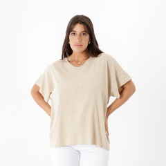 Modelo usando una blusa de color beige, con mangas cortas y un diseño simple, en un fondo blanco.