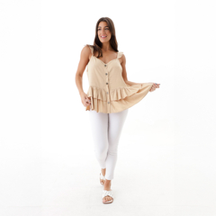 Modelo luciendo una blusa Aria de color beige con botones frontales y un diseño con volantes, combinada con pantalones blancos.