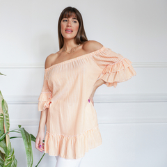 Blusa Ariadna de rayas en color melocotón, con mangas acampanadas y detalles de volantes, modelo femenino posando frente a una pared blanca.