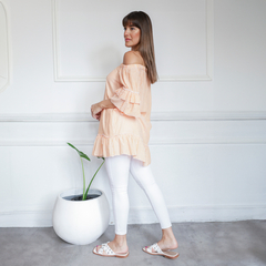 Modelo luciendo una blusa de rayas en tonos melocotón, con mangas acampanadas y un diseño fluido, combinada con pantalones blancos y sandalias.