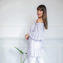 Blusa Ariadna de tirantes off-shoulder con volantes, en color lila, usada por una mujer de perfil.