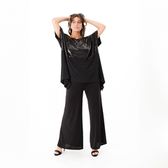 Model luciendo una blusa negra con detalles brillantes, combinada con pantalones amplios y tacones.