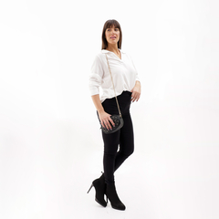 Modelo luciendo una blusa blanca Ceylu, combinada con pantalones negros y botas de tacón, posando con un bolso negro.