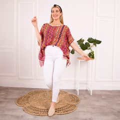 Modelo luciendo una blusa cirque de diseño colorido, combinada con pantalones blancos, en un ambiente luminoso con decoración minimalista.
