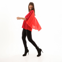 Modelo luciendo una blusa roja con mangas amplias, acompañada de pantalones negros ajustados y tacones, en un fondo blanco.