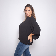Modelo luciendo una blusa negra de corte amplio y mangas acampanadas, combinada con jeans azules.