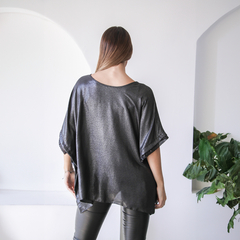 Blusa Ginebra de color negro con brillo, vista desde atrás, combinada con pantalones ajustados y decoraciones en las mangas.