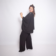 Modelo usando una blusa negra Idalis con pantalones negros, posando de lado en un fondo blanco.