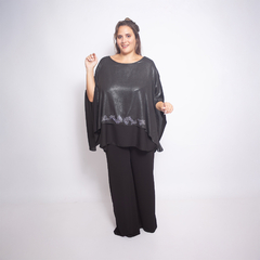 Modelo usando una blusa negra brillante con detalles en la parte inferior, combinada con pantalones negros.