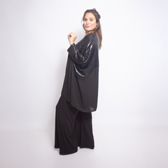 Modelo luciendo una blusa negra con detalles brillantes, combinada con pantalones oscuros.