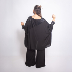 Blusa Idra negra con detalles brillantes, vista trasera de una modelo con pantalones amplios.