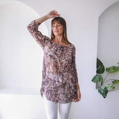 Blusa Iris de manga larga, con estampado en tonos marrones y detalle de volados en la parte inferior, modelo posando en un ambiente luminoso.