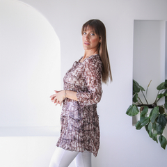 Modelo luciendo una blusa Iris de estampado marrón, con un fondo minimalista y plantas verdes.