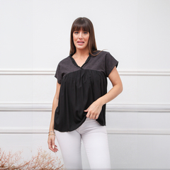 Modelo luciendo una blusa negra con detalles en la parte superior, combinada con pantalones blancos.
