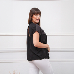 Modelo luciendo una blusa negra con detalles en la espalda, combinada con pantalones blancos.
