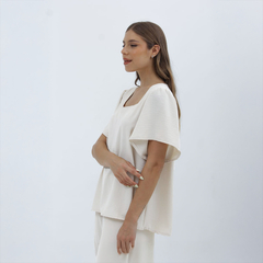 Blusa Nalani de color blanco, con mangas amplias y corte recto, presentada en una modelo de perfil.