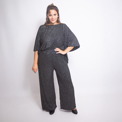 Modelo usando una blusa negra brillante y pantalones anchos, posando con una mano en la cadera.