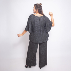 Modelo luciendo una blusa negra con brillo desde la parte posterior, combinada con pantalones anchos.