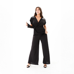 Modelo vistiendo una blusa negra Rem con detalles en el escote, combinada con pantalones anchos.