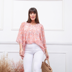 Modelo usando una blusa de estampado floral en tonos rosados, combinada con pantalones blancos y un bolso de mimbre.