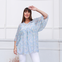 Modelo usando una blusa liviana de estampado en tonos azules con mangas amplias, posando con una mano en la frente.