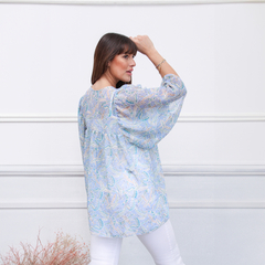Blusa Siena de estampado floral en tonos azules, vista posterior de una modelo que lleva pantalones blancos.