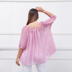Vista trasera de una blusa rosa con estampado de flores, de manga larga y holgada, sobre fondo blanco.