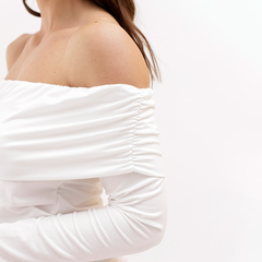 Mujer con blusa blanca de manga larga y escote off-shoulder, mostrando un estilo elegante y moderno.