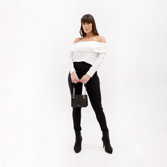 Modelo de pie luciendo una blusa blanca de hombros descubiertos y pantalones negros ajustados, sosteniendo un bolso negro.