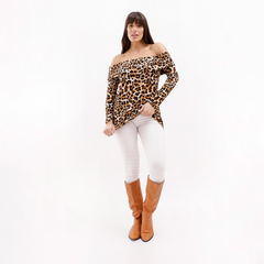 Mujer posando con una blusa de leopardo sin mangas y pantalones blancos, usando botas marrones.
