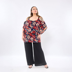 Mujer con blusa Bella estampada de flores rojas y beige sobre fondo azul, combinada con pantalón negro ancho y sandalias