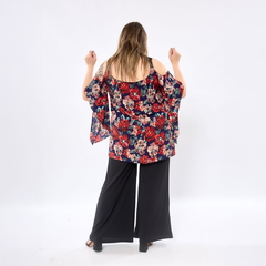 Vista trasera de mujer con blusa Bella estampada de flores rojas y beige, mangas amplias y hombros descubiertos, combinada con pantalón negro ancho