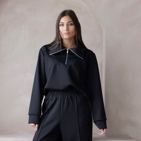 Buzo negro Valencia con cierre frontal y cuello amplio, modelo femenino posando