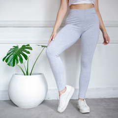 Calza básica chupín gris, ajustada, combinada con una camiseta y zapatillas blancas, junto a una planta en maceta blanca.