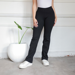 Calza básica recta de color negro, usada por una mujer que posa junto a una planta decorativa en una habitación moderna.