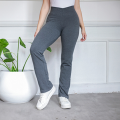 Calza básica recta en color gris, con una mujer de pie mostrando el diseño, junto a una planta en maceta blanca.