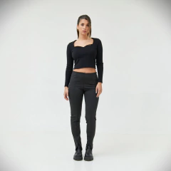 Modelo femenina posando con un conjunto de ropa negra que incluye una blusa de manga larga y pantalones ajustados.