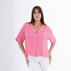 Modelo luciendo una camisa clavel de color rosa, con botones y cuello, combinada con pantalones blancos.