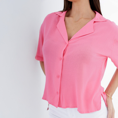 Camisa Clavel de color rosa, con botones y cuello, usada por una mujer con pantalones blancos.