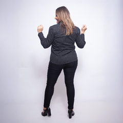 Vista trasera de una mujer usando una camisa de rayas en tonos oscuros y pantalones negros.