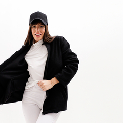 Mujer sonriendo mientras lleva puesta una campera negra abierta, con una camiseta blanca y una gorra negra.