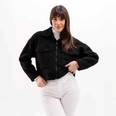 Modelo usando una campera negra de estilo cropped, con cierre y dos bolsillos frontales, combinada con una camiseta blanca y pantalones claros.