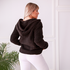 Campera Keira de color negro vista desde atrás, con capucha y textura suave, combinada con pantalones blancos.