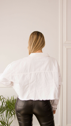 Vista posterior de una campera blanca de estilo cropped, combinada con pantalones ajustados oscuros.