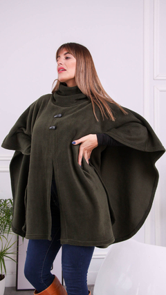 Mujer modelando una capa Marano de color verde oliva, con cierre en el frente y bolsillos laterales. Fondo neutro y decoración minimalista.