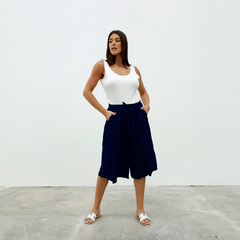 Mujer posando con un top blanco y pantalones cortos azul marino, en un fondo blanco.