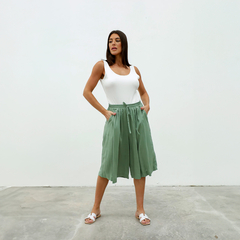 Pantalones Capri Dayak de color verde, con una modelo posando en un fondo blanco, usando una camiseta blanca y sandalias.