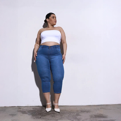 Mujer con top blanco y pantalones de mezclilla azul, posando frente a una pared blanca.